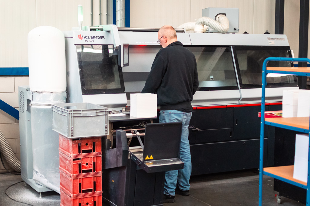 Productiemedewerker machinale nabewerking aan het werk bij een machine voor het lijmen van de ruggen van boeken