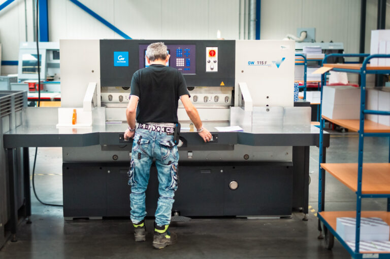 Productiemedewerker machinale nabewerking aan het werk bij een snijmachine